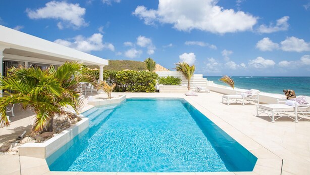 Une piscine avec vue sur l’océan, entourée de chaises longues et de palmiers.