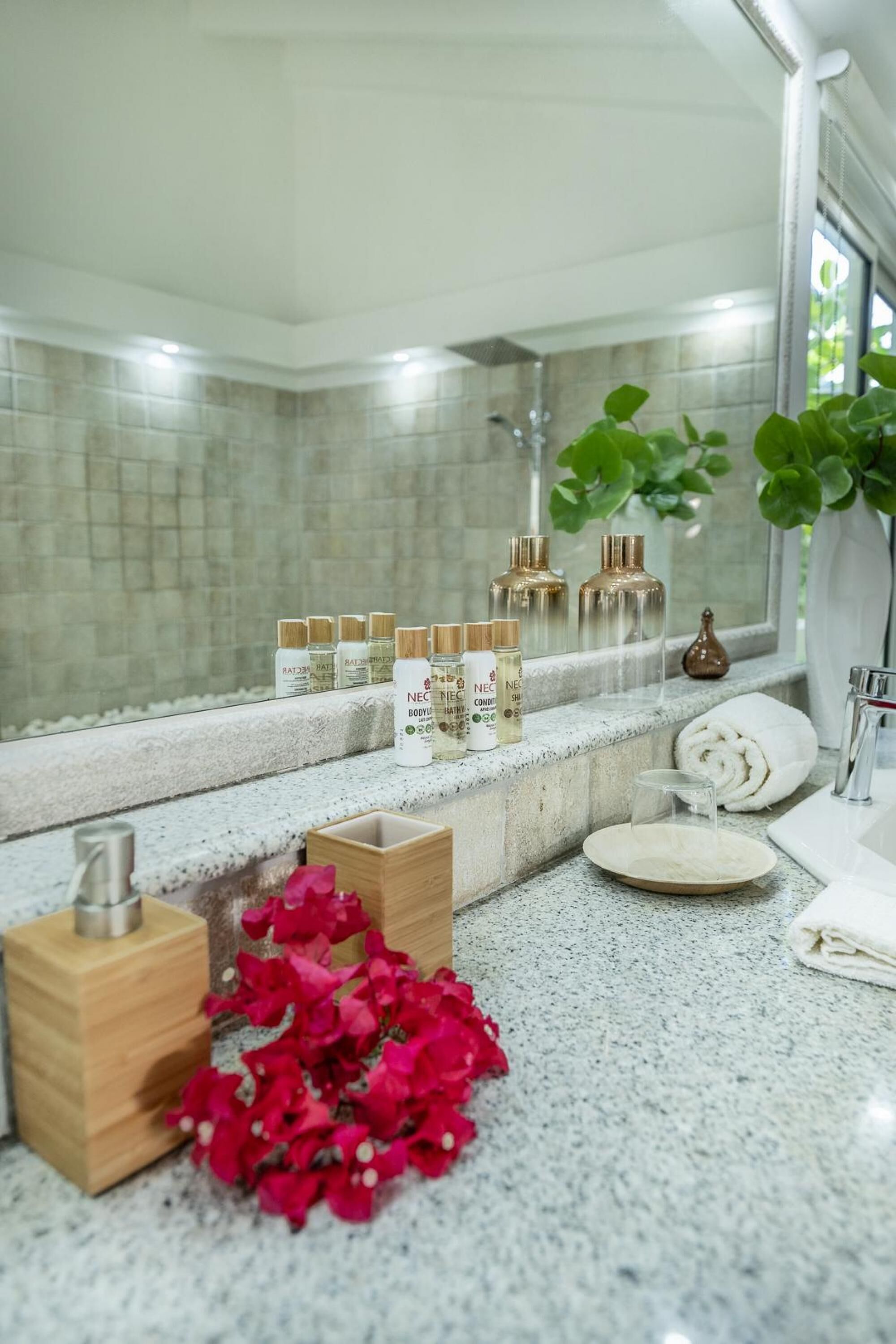 A bathroom with a granite countertop, a wooden box, and a vase with red flowers.