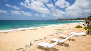 Une plage avec des chaises longues blanches et une vue dégagée sur l’océan.