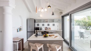 Une cuisine moderne dotée d’un îlot central, de luminaires suspendus et d’une grande porte-fenêtre coulissante donnant sur un patio extérieur.
