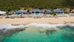A beachfront property with multiple pools, a sandy beach, and a rocky shoreline.