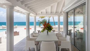 A covered outdoor area with a pool, white furniture, and a view of the ocean.