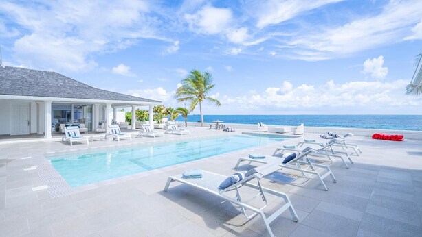 A poolside area with lounge chairs, a covered seating area, and a view of the ocean.