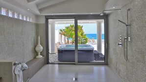 A modern bathroom with a large sliding glass door leading to a balcony with a hot tub and a view of the ocean.