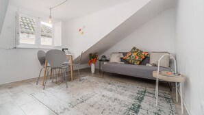 A modern loft bedroom with a sloped ceiling, a gray sofa with floral cushions, a small table with a magazine, and a desk with a chair. - Nomad s Castel Lisbon - 1bdr The Reader (Lisbon)