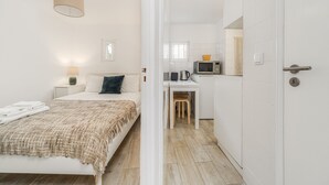 A compact hotel room with a bed, bedside table, lamp, and a kitchenette area with a microwave and kettle. - Nomad s Castel Lisbon - 1bdr The Reader (Lisbon)
