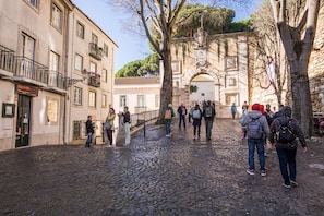 A cobblestone street with people walking, historic buildings, and a large archway. - Nomad s Castel Lisbon - 1bdr The Reader (Lisbon)