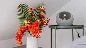 A white vase with orange flowers and green leaves on a wooden floor, next to a green metal table with a lamp. - Nomad s Castel Lisbon - 1bdr The Reader (Lisbon)