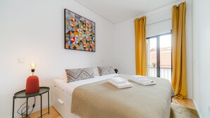A bedroom with a bed, a bedside table with a lamp, a colorful geometric artwork on the wall, and a window with yellow curtains. - Nomad s Netto Subway - Sunny Balcony (Porto)