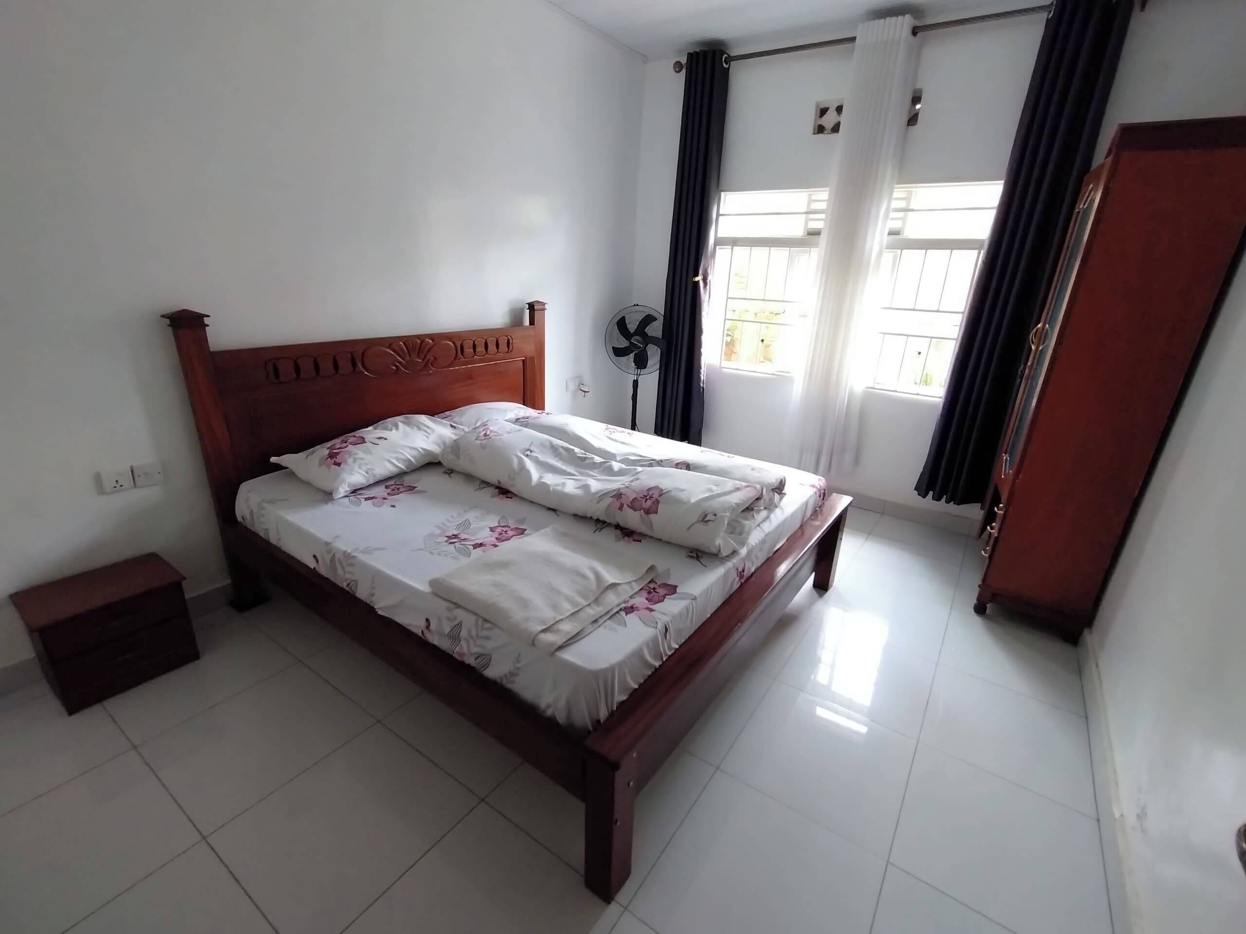 Una cama bien tendida con ropa de cama estampada en una habitación con paredes blancas y suelo de baldosas.