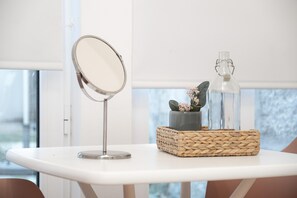 A white table with a round mirror and a woven basket containing a vase with flowers and a clear bottle. - Nomad s Boulevard Flats - Suite Terrace 1 (Porto)