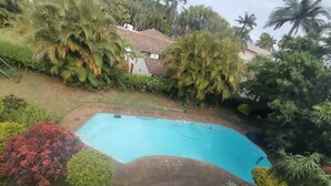 A swimming pool surrounded by lush greenery and a house in the background. - Luxury Flatlet in the heart of Umhlanga (uMhlanga)