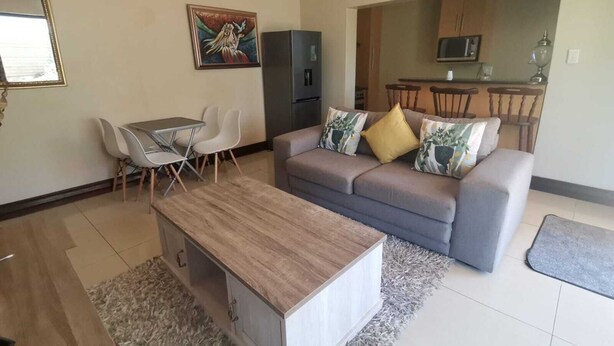 A modern living room with a grey sofa, a wooden coffee table, and a dining area with a small table and chairs. - Luxury Flatlet in the heart of Umhlanga (uMhlanga)