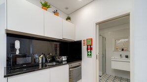 A modern kitchen with white cabinets, a black countertop, a microwave, a stove, and a sink. There are potted plants on the ceiling and a fire extinguisher on the wall. - Nomad s Netto Subway - Lovely Terrace (Porto)