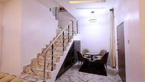 Un intérieur moderne avec un escalier, un coin repas comprenant des chaises et une table, et un luminaire au plafond.