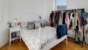 A bedroom with a bed, a nightstand, a dresser, a window, and a clothing rack. - Apartment Sleeps 2 with Free Parking (London)