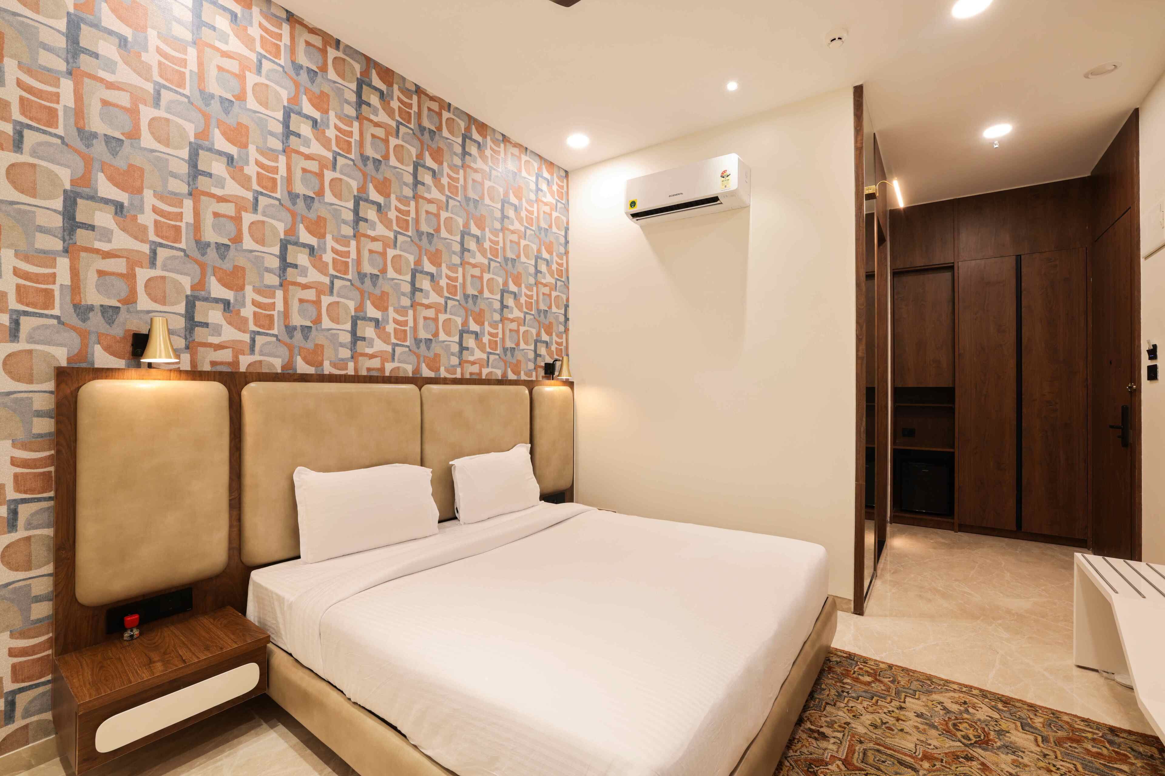 Quarto de hotel bem arrumado com parede estampada, cama com lençóis brancos, mesa de cabeceira com abajur e guarda-roupa.