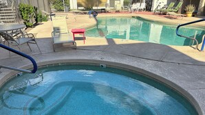 Ein Whirlpool mit Fliesenrand, ein Schwimmbecken und Liegestühle darum herum.