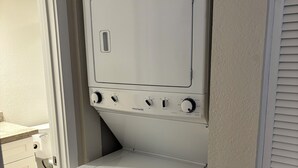 Ein kleiner Waschraum mit einer Frontlader-Waschmaschine und -Trockner, einer kleinen Arbeitsplatte und einer Tür zu einem anderen Raum.