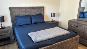 Ein Bett mit Holz Kopfteil, zwei Nachttische mit Lampen, eine Kommode und ein Spiegel.