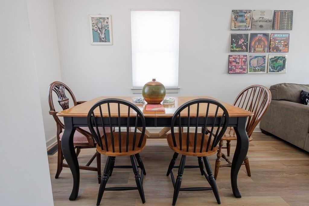 A dining table with four chairs, a vase, and a window with blinds.
