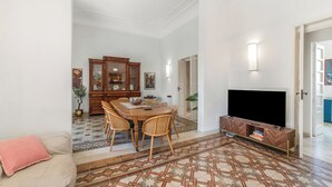 A living room with a TV, a dining area with a wooden table and chairs, and a patterned floor.