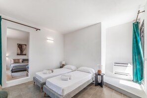 Habitación de hotel con dos camas, una mesita, una lámpara, un cuadro en la pared y una ventana con cortinas.
