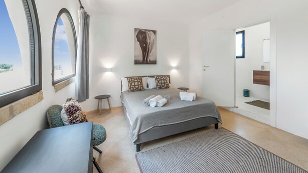 A bedroom with a bed, a desk, a chair, a window, and a door.