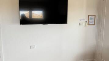 Una habitación con televisión montada, suelo de madera, sofá gris y una alfombra pequeña.