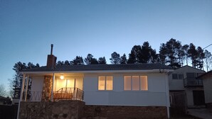 Ein eingeschossiges Haus mit steinernen Fundament und weißer Fassade. Es verfügt über eine Veranda mit Geländer und eine Treppe, die zum Eingang führt.