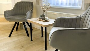 Ett modernt vardagsrum med två grå fåtöljer, ett soffbord i trä och en vas med blommor.