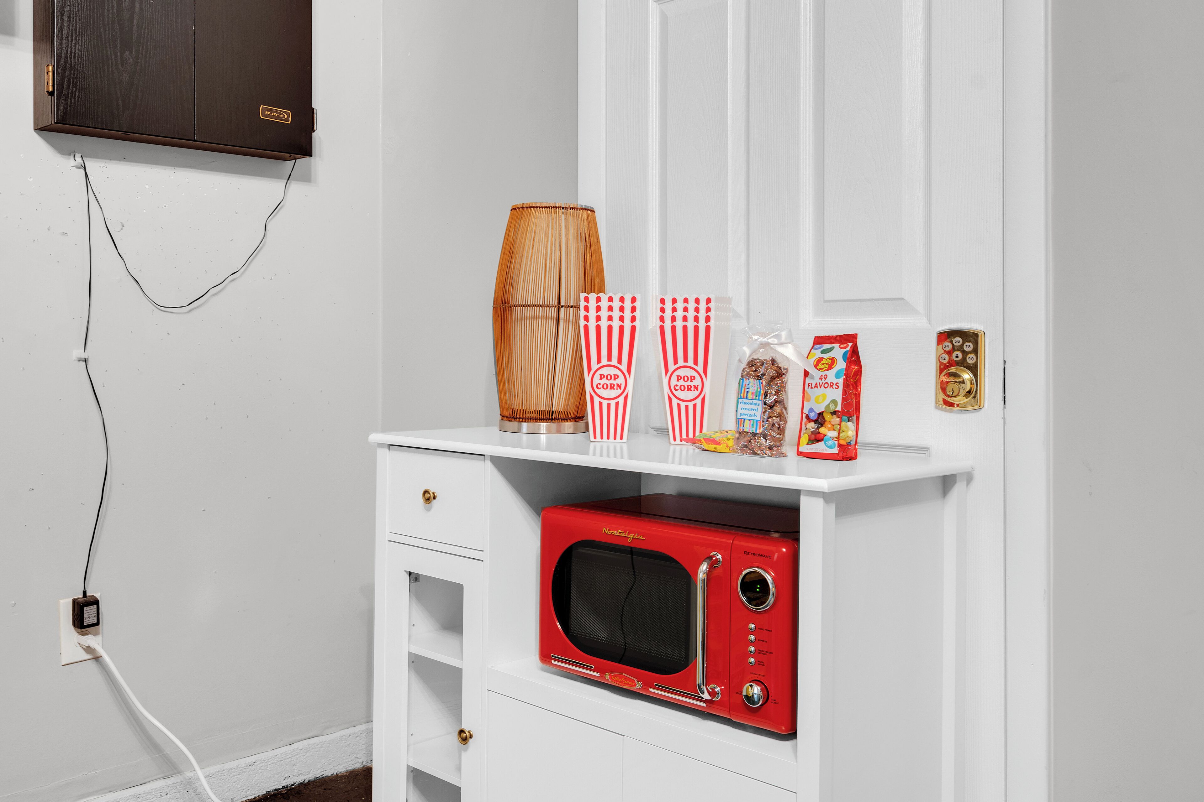 A white cabinet with a red microwave, popcorn containers, and a popcorn machine on top.