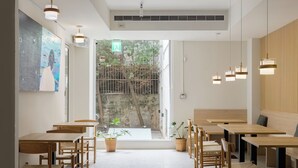 L’intérieur d’un café moderne, avec des tables et des chaises en bois, des plantes en pot et une grande fenêtre donnant sur une cour.