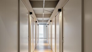 Un couloir moderne avec un plancher en bois et des murs blancs, qui mène à une pièce lumineuse dotée d’une grande fenêtre.