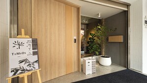 L’entrée d’un hôtel, avec une porte en bois, un comptoir d’accueil, une plante en pot et un panneau indicateur.