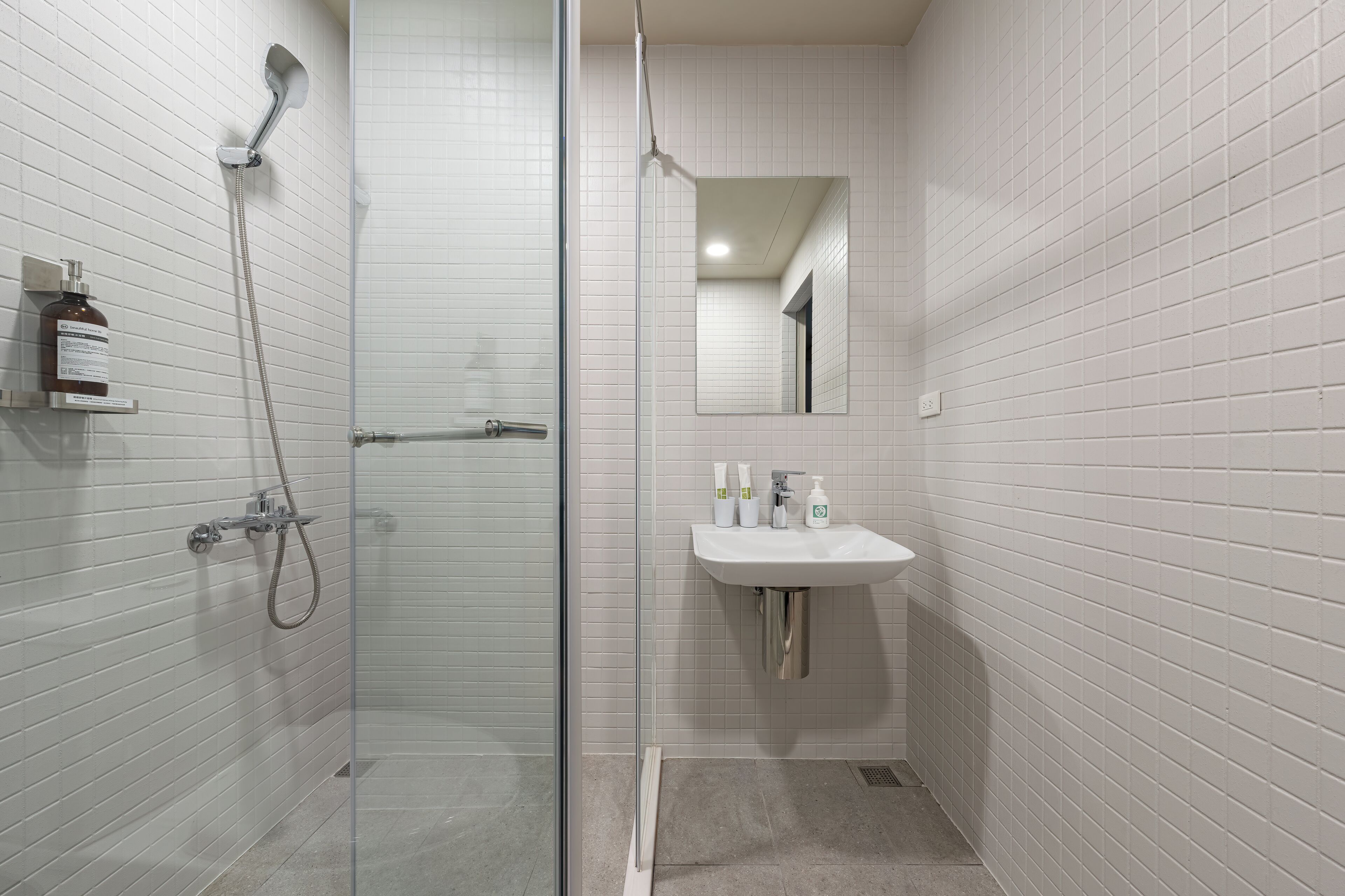 Un baño moderno con cabina de ducha de vidrio, un lavamanos blanco con artículos de aseo y un espejo en la pared.