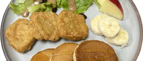 A plate with pancakes, apple slices, banana slices, a salad with dressing, and fried items.