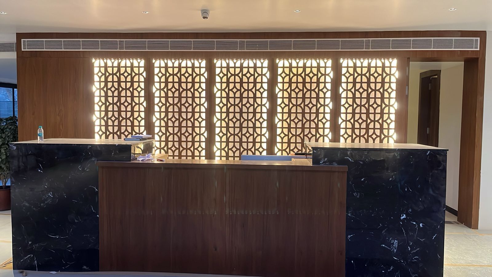 A reception desk with a wooden finish and a marble top, flanked by a decorative screen with geometric patterns.