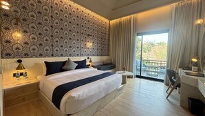 Quarto de hotel com uma cama grande, uma escrivaninha pequena, uma cadeira, uma mesa redonda e uma varanda com vista.