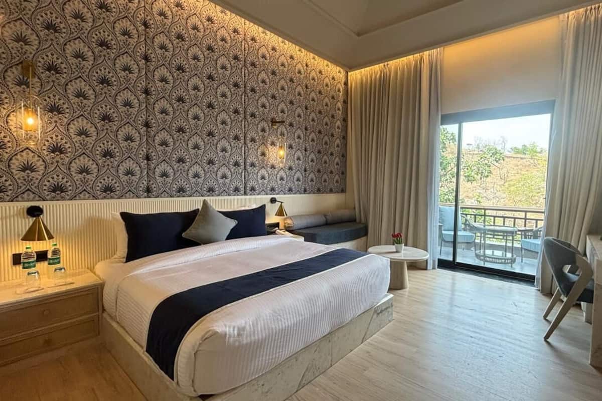 Ein Hotelzimmer mit einem großen Bett, einem kleinen Schreibtisch, einem Sessel, einem runden Tisch und einem Balkon mit Blick.