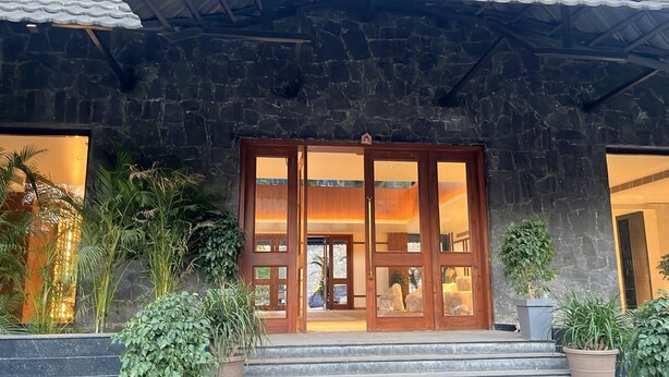 Um edifício de pedra com uma grande entrada de madeira, plantas em vasos e vista para o interior.