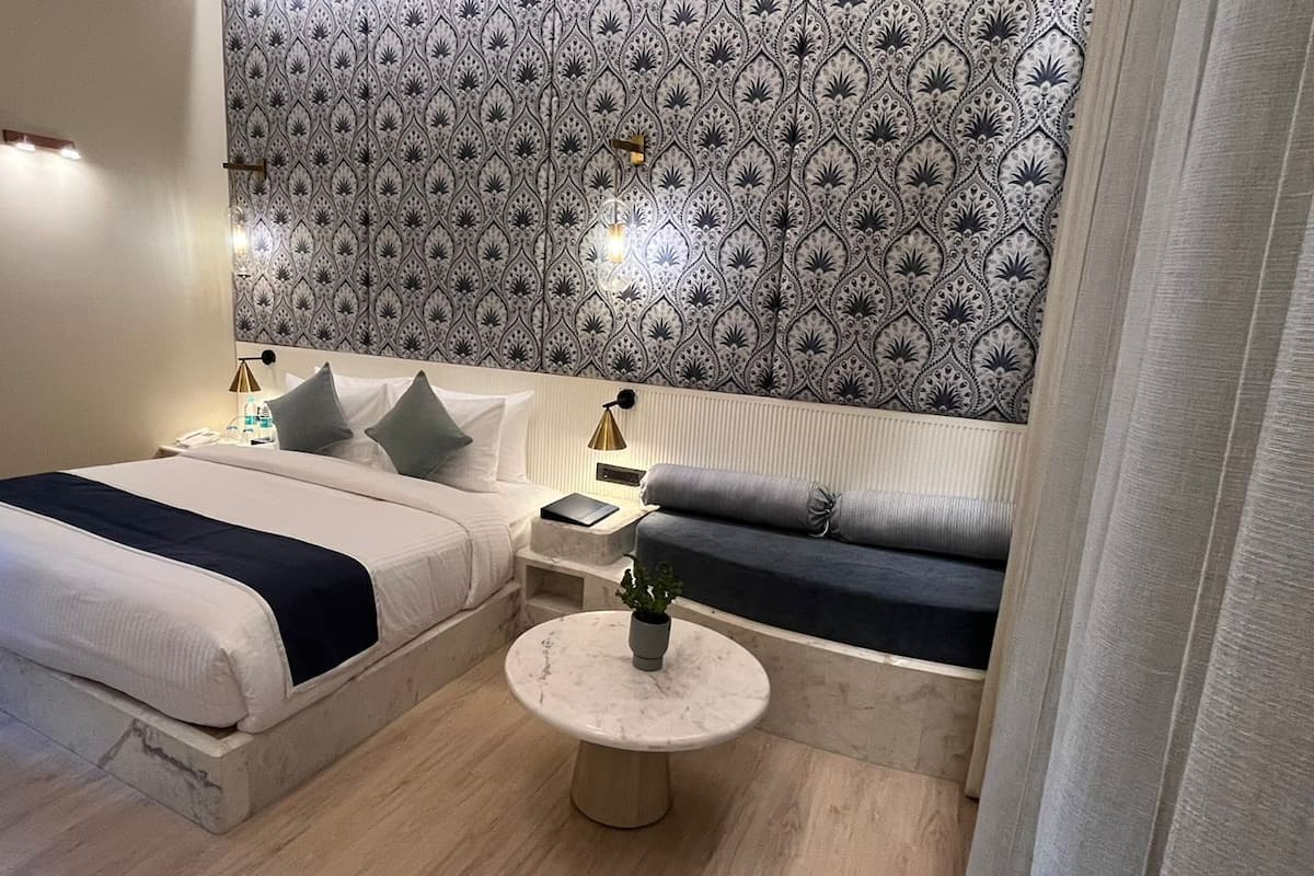 Ein modernes Schlafzimmer mit einem Bett, Nachttischen, einem Sofa und einem kleinen runden Tisch mit einer Pflanze.