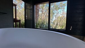 A room with a large window, a white bathtub, and a wooden chair.