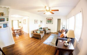 A spacious living room with hardwood floors, a ceiling fan, and a dining area with a table and chairs. - The Blue Jay House in North Fondren (Jackson)