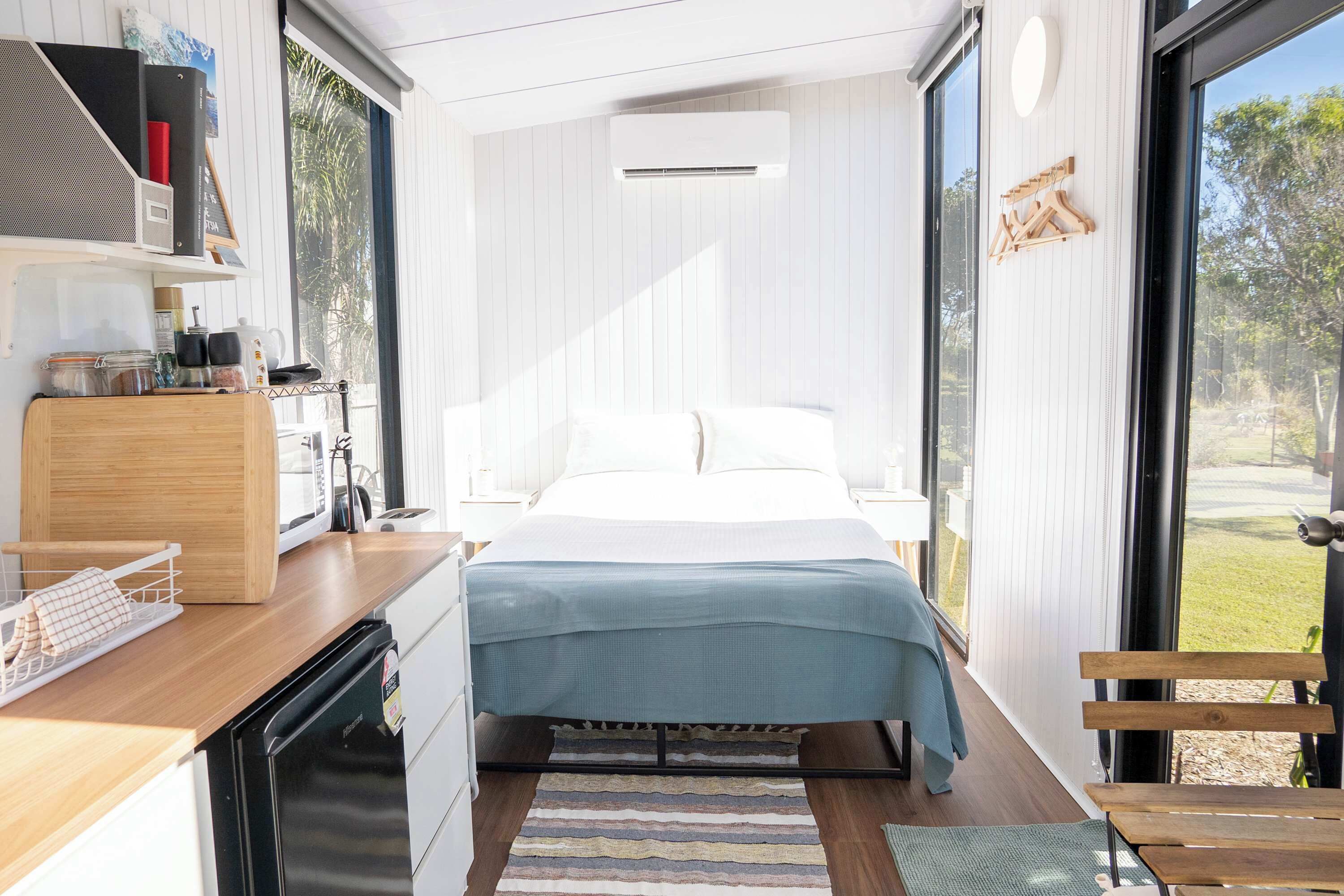 Ein modernes Schlafzimmer mit einem Bett, einem Holztisch, einem eingebauten Geschirrspüler und einem großen Fenster.