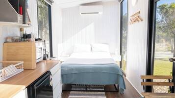 Ein modernes Schlafzimmer mit einem Bett, einem Holztisch, einem eingebauten Geschirrspüler und einem großen Fenster.