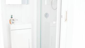 Casa de banho com lavatório branco, espelho e cabine de duche em vidro.