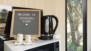 A sign reading "WELCOME TO CATHEDRAL VIEWS" on a blackboard, a black coffee maker, and two white cups on a counter.
