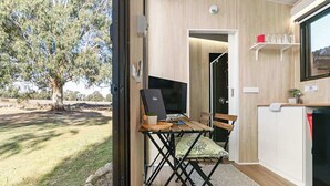A room with a desk, chair, and a television. There is a window with a view of a tree and a building.