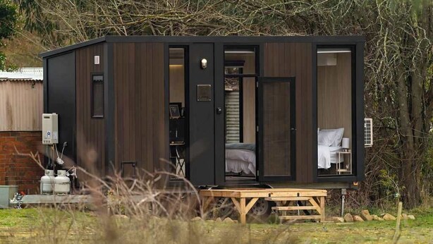 A compact, modern cabin with a wooden exterior, a single visible bedroom with a bed, and a small porch area.